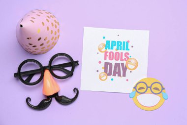 NİSAN FOOLS GÜNÜ yazılı kart, parti şapkası ve eflatun arka planda komik kılık değiştirme