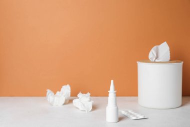 Turuncu duvarın yanındaki masada burun damlası ve peçete kutusu var. Alerji konsepti