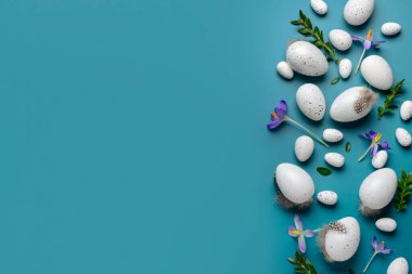 Paskalya yumurtaları, güzel kır çiçekleri ve mavi arka planda bitki yaprakları.