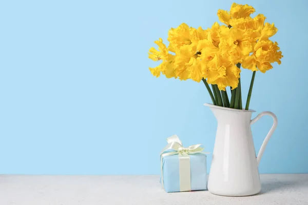 stock image Vase with narcissus flowers and gift on table near blue wall
