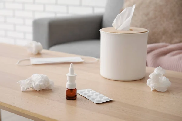 Nasal drops with pills and tissue box on table in living room, closeup. Allergy concept