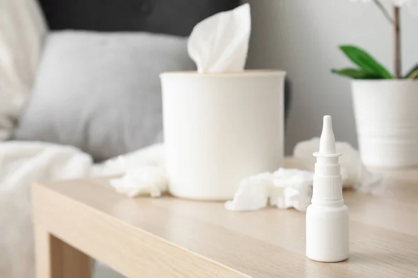 Nasal drops with tissue box on table in living room, closeup. Allergy concept