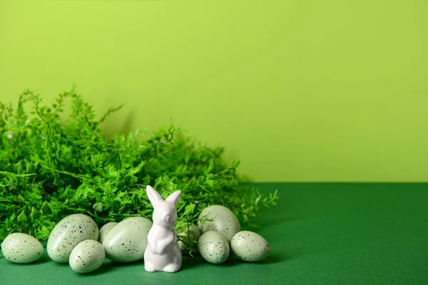 stock image Easter eggs, porcelain bunny and plant leaves on green background