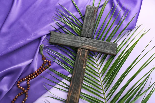 stock image Wooden cross with palm leaf, prayer beads and purple fabric on lilac background. Good Friday concept