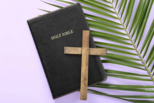 stock image Wooden cross with Holy Bible and palm leaf on lilac background. Good Friday concept