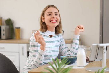 Young woman having breakfast at table in kitchen