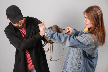 Young woman with pepper spray defending herself against thief on grey background