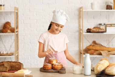 Küçük fırıncı mutfaktaki çöreklerin üzerine şeker serpiyor.