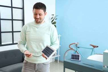 Yakışıklı adam cep telefonunu taşınabilir güneş paneliyle şarj ediyor.