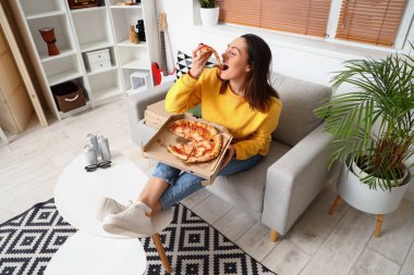 Evdeki kanepede oturan bir kutu lezzetli pizzayla güzel bir kadın.
