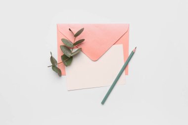 Beyaz arkaplanda boş kart, zarf, kalem ve okaliptüs dalı