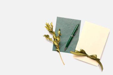 Beyaz arkaplanda boş kart, zarf, kalem ve bitki dalı olan kompozisyon