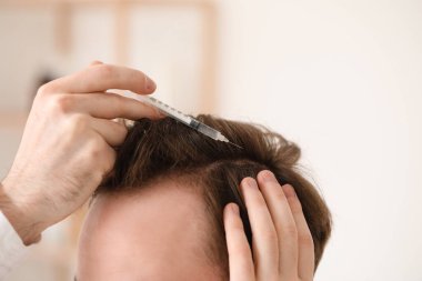 Banyoda saç uzatmak için iğne yaptıran genç adam, yakın plan.