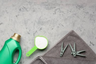 Çamaşır deterjanları, çamaşır mandalları ve gri grunge arka planda havlu.