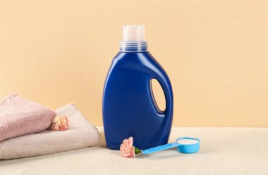Çamaşır deterjanları, karanfil çiçekleri ve katlanmış havlular bej arka planda.