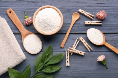 Çamaşır deterjanları, mandallar, karanfil çiçekleri ve gri ahşap arka planda bitki dalları.