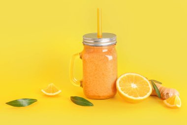 Sarı arka planda saman bulunan sağlıklı portakal suyu kavanozu.