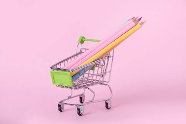 Pembe arka planda kalemleri olan alışveriş arabası.