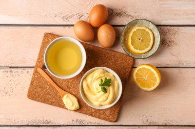 Lezzetli mayonez soslu kase ve hafif ahşap arka planda malzemeler.