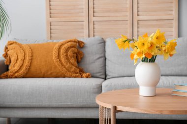 Oturma odasındaki sehpanın üzerinde narsis çiçekleri olan vazo.