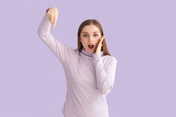 Zszokowana Młoda Kobieta Swetrze Wskazująca Coś Liliowym Tle — Zdjęcie stockowe
