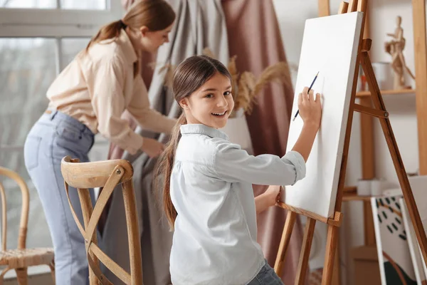 Little girl learning to draw with teacher near easel in workshop