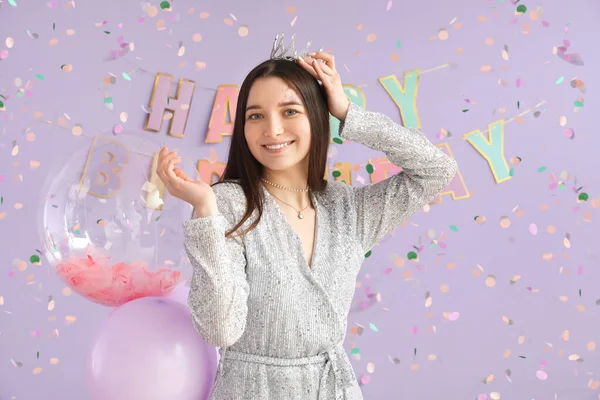Happy young woman in crown celebrating Birthday on lilac background