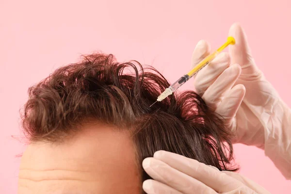 Young man receiving injection for hair growth on pink background, closeup