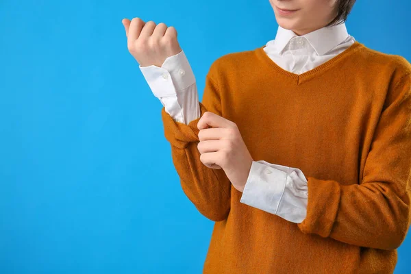 Teenage boy rolling up his sleeve on blue background, closeup