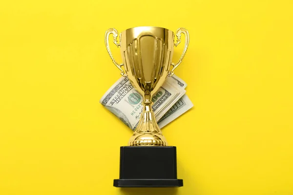 Gold cup with money on yellow background