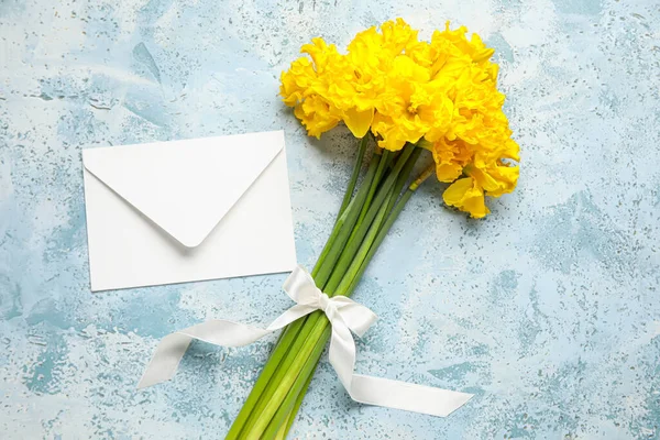 Beautiful narcissus flowers with ribbon and envelope on color background