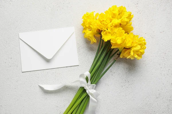 Beautiful narcissus flowers with ribbon and envelope on light grunge background