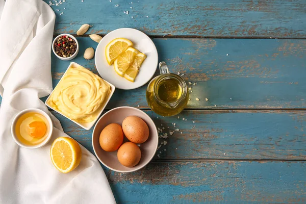 stock image Bowl with tasty mayonnaise sauce and ingredients on color wooden background