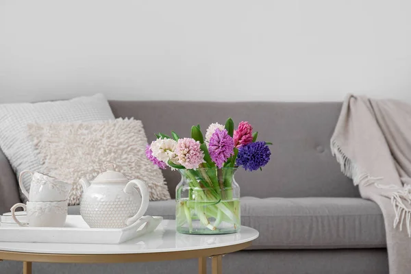 Vase with hyacinth flowers, teapot and cups on coffee table in living room