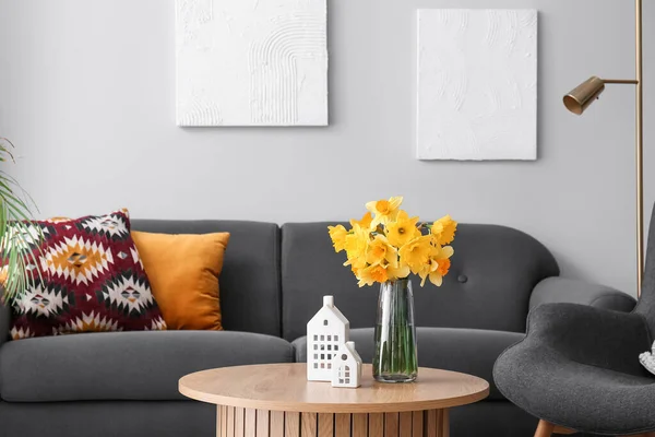 リビングのソファの近くのコーヒーテーブルの上に磁器の家や花瓶の花 — ストック写真