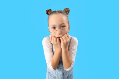 Stressed little girl biting nails on blue background