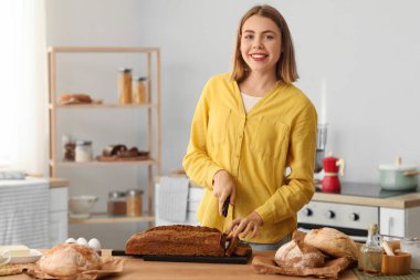 Young woman cutting rye bread at table in kitchen