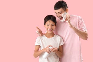 Man and his little son applying shaving foam onto faces against pink background