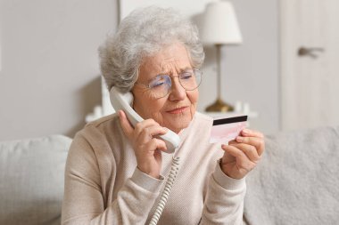 Kredi kartıyla evde telefonla konuşan yaşlı bir kadın, yakın plan.