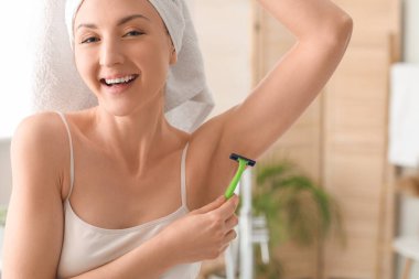 Genç ve güzel bir kadın banyoda koltuk altlarını tıraş ediyor.