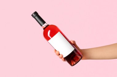 Pembe arka planda kırmızı şarap şişesini tutan kadın.