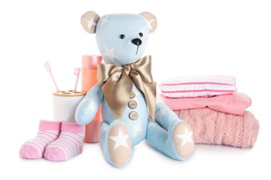 Beyaz arka planda bebek kıyafetleri ve aksesuarları olan oyuncak ayı.