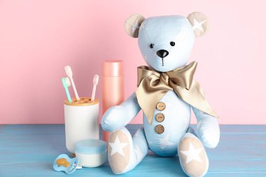 Bebek aksesuarlı oyuncak ayı pembe duvarın yanında.