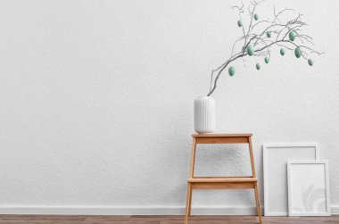 Ağaç dallı vazo, Paskalya yumurtaları ve ışık duvarının yanındaki boş resim çerçeveleri.