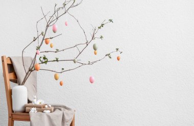 Ağaç dalları olan vazolar, Paskalya yumurtaları ve ışık duvarının yanındaki sandalyede kitaplar.