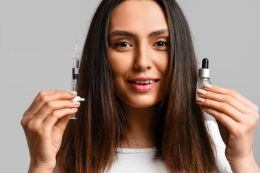 Saç dökülmesi tedavisi için serum ve gri arka planda şırınga olan güzel bir kadın.