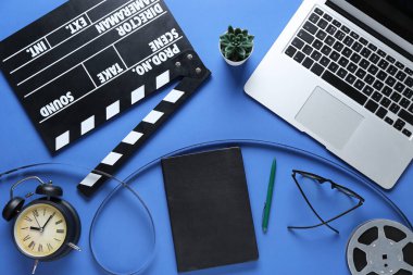 Mavi zemin üzerinde film, alarm saati, film makarası ve dizüstü bilgisayarı olan bir defter.