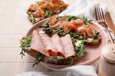 Pastırma, jambon ve arkaplanda roka olan jambon bruschetalar.