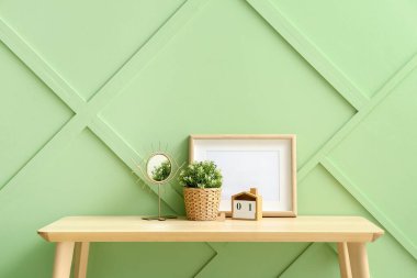 Ayna, takvim ve boş çerçeveli yapay ev bitkisi yeşil duvarın yanında.