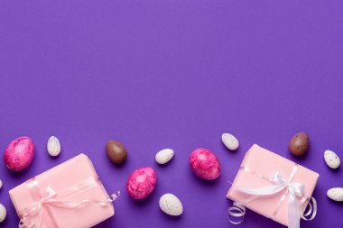 Paskalya yumurtaları ve mor arka planda hediye kutularıyla kompozisyon
